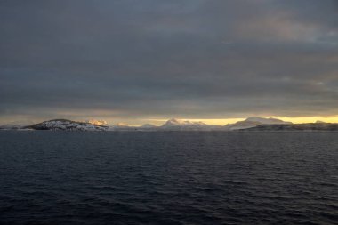 Norveç denizinin sakin suları. Karla kaplı dağlar, kutup gündoğumunda parlak sarı renkler. Renkli gökyüzü. Harstad, Norveç.