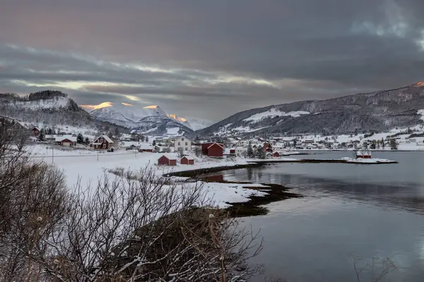 Norveç denizinin körfezi. Sahilde evler ve arka planda dağlar var. Kuzey Kutbu 'nda gün doğumunda güneş ışığının dokunduğu yerler. Bulutlu gökyüzü. Harstad, Norveç.