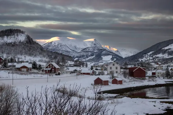 Norveç denizinin körfezi. Sahilde evler ve arka planda dağlar var. Kuzey Kutbu 'nda gün doğumunda güneş ışığının dokunduğu yerler. Bulutlu gökyüzü. Harstad, Norveç.