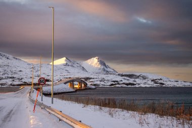 Kuzey Kutbu 'nda gün batımında kar manzarası. Norveç denizinden Sansoya adasına giden köprü. Renkli gökyüzü. Tjeldevika, Norveç.