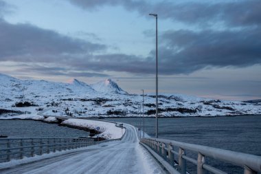 Kuzey Kutbu 'nda gün batımında kar manzarası. Norveç denizinden Sansoya adasına giden köprü. Renkli gökyüzü. Sandsoy, Norveç.