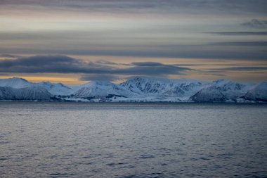 Norveç denizi ve dağları ufuktaki Kuzey Kutbu sonbaharında karla kaplıydı. Gün batımında gökyüzü renklidir. Grotavaer, Grytoya, Norveç.
