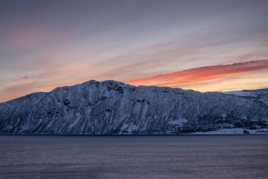 Kuzey Kutbu sonbaharında ufukta karla kaplı Norveç denizi ve dağları. Gün batımında gökyüzü renklidir. Grotavaer, Grytoya, Norveç.