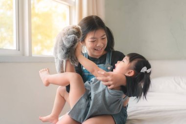 Büyük Asyalı kız kardeş ve küçük Asyalı kız kardeş hayvani el kuklası oyuncakları oynuyorlar, yatakta oturuyorlar, anaokulu oyunları oynuyorlar ev kavramındaki çocukla eğleniyorlar..;