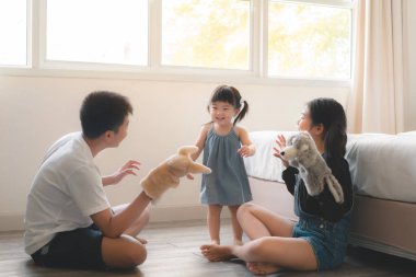 Asyalı abla ve abla, küçük Asyalı kız kardeşle el kuklası oyuncakları oynuyorlar, yatağın yanında oturuyorlar, anaokulu oyunları oynuyorlar, ev konseptinde çocuklarla eğleniyorlar..