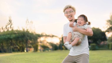 Asyalı bir baba kızıyla parkta yürürken ebeveynler bebeğini elinde tutarken mutlu bir aile parkın akşam ışığında. Mutlu aile kavramı.