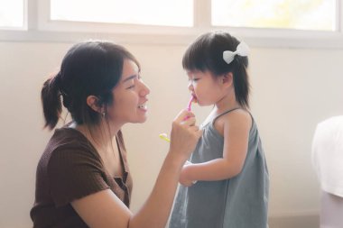 Asyalı anne ve kızı birlikte dişlerini fırçalarken, annesi kızına diş fırçalamayı öğretirken, ağızdan sağlık kavramı öğretirken,