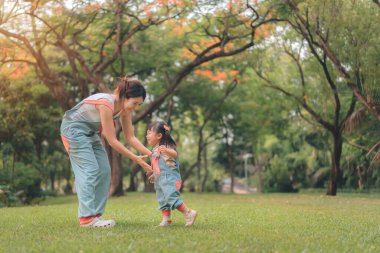 Asyalı anne kızıyla parkta yürüyor, mutlu aile parkın akşam ışığında, mutlu aile kavramı..