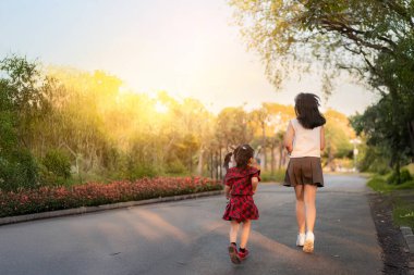 Ablam ve küçük kız kardeşim gün batımında parkta birlikte koşuyorlar. Yumuşak güneş ışığı ve doğal çevre sıcak ve mutlu bir atmosfer yaratıyor, aile bağlarını ve sağlıklı bir yaşam tarzını gösteriyor..