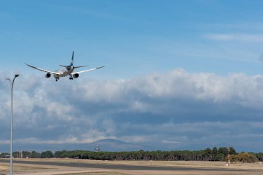 Büyük ticari uçak Adolfo Suarez havaalanının pistine inmeye hazır gri bulutlarla kaplı bir gökyüzünün altında.
