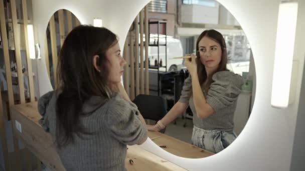 鏡を見ながらサロンに顔に粉を広げる大人の女性の高角度ハンドヘルドショット — ストック動画