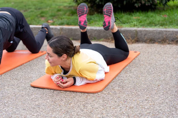 Full body of young female athlete with bun hairstyle in sportswear lying on orange yoga mat and stretching legs in park