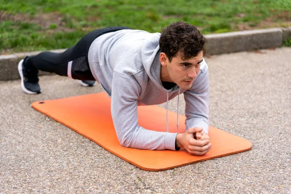 Full body of concentrated male athlete in activewear doing plank exercise on orange mat in park