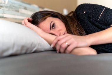 side view of sad brunette young woman lying in bed, having mental problem sick with depression