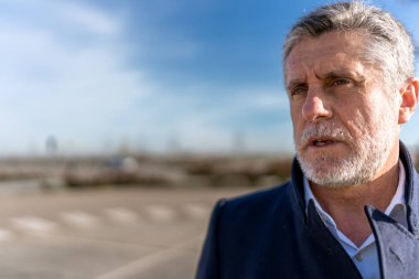 Serious mature bearded businessman in formal wear looking away thoughtfully while standing on street