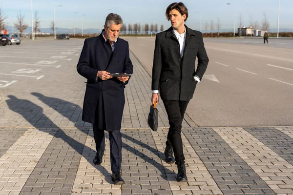 Full body of serious businessmen in classy clothes walking on paved street and talking to each other while discussing business plan