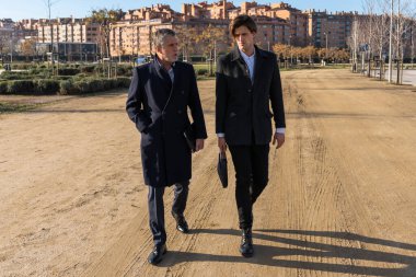 Full body of serious businessmen in formal clothes walking on street together while discussing business strategy