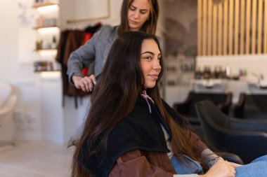 Focused female stylist combing long hair of client while preparing for beauty procedure in hairdressing salon
