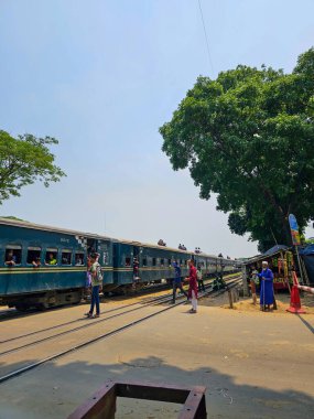 Dhaka, Bangladeş - 01.06.2023: Tren öğle saatlerinde hareket halindeyken trenin geçmesi için tren sinyali bekleyen insanlar.