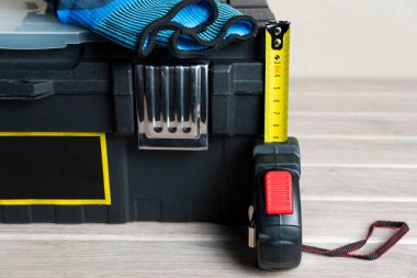 Üzerinde mavi ve siyah iş eldivenleri ve genişletilmiş sarı bir mezura olan siyah bir alet çantası DIY projeleri ve ev onarımı için hazır.