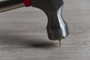 Altında bir iğne bulunan metal çekiç başının detaylı bir yakın çekimi, ahşap bir yüzeyde dinleniyor, dokuyu ve keskinliği vurguluyor.