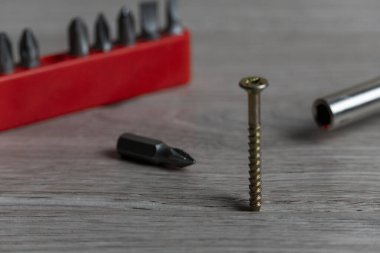 Kırmızı bir tutacaktaki çeşitli tornavida parçalarının detaylı yakın plan görüntüleri ve tek bir vida desenli ahşap bir yüzey üzerinde duruyor. Onarım ve DIY projeleri için hassas aletler ve donanım unsurları gösteriliyor.