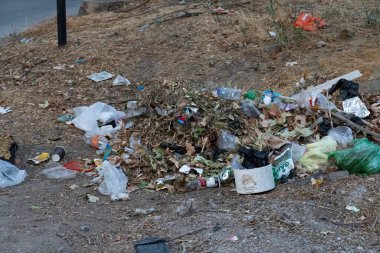 İçinde plastik torbalar, şişeler, teneke kutular ve kirli şehir zemininde kuru yapraklar olan çöp yığını. Şehir sokaklarında çöp ve çevre kirliliği kavramı