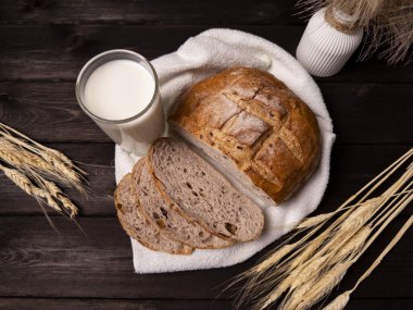 İçinde taze pişmiş ekmek, dilimlenmiş ve yanında bir bardak süt bulunan rahat bir hayat. Buğdaylı kırsal ortam biraz sıcaklık katıyor, yiyecekle ilgili içerik için ideal.