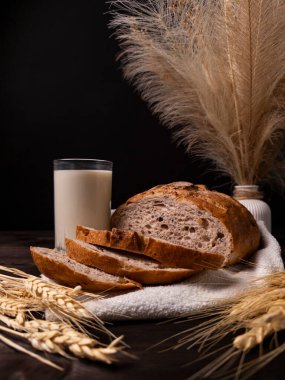 Bir bardak sütle birlikte taze pişmiş köy ekmeği ve sıcak ve davetkar bir atmosfer yaratan zarif buğday dekoru.