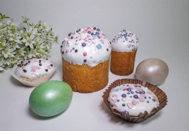 Renkli serpiştirilmiş geleneksel Paskalya pastaları, boyalı yumurtalar ve beyaz arka planda bahar çiçekleri.