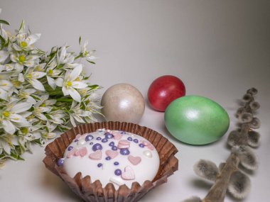 Traditional Easter composition with a decorated cupcake, painted eggs, spring flowers, and pussy willow on a white background