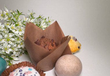 Beyaz bahar çiçekleri, Paskalya yumurtaları ve bayramlık tatlı ekmekle çevrili kahverengi kağıttan ambalajlı çikolatalı kek. Hafif bir arkaplanda sezonluk tatil kompozisyonu