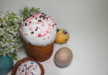 Geleneksel paskalya pastası beyaz kremalı, pembe serpiştirmeli, boyalı yumurtalı ve açık arkaplanda beyaz bahar çiçekleri. Şenlikli natürmort kompozisyonu