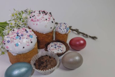 Geleneksel pastalarla, boyalı yumurtalarla, söğüt dallarıyla, beyaz çiçeklerle ve arka planda çeşitli kekleri olan Paskalya kompozisyonu.