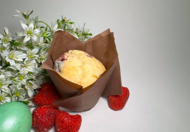 Beyaz bahar çiçekleri, çilekler ve yeşil boyalı Paskalya yumurtası ile çevrili kahverengi parşömen kağıdında ev yapımı meyveli kek. Şenlikli ve kırsal pastane natürmort