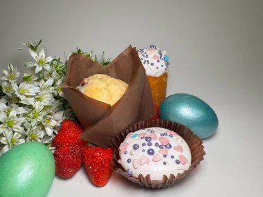 Kapkeklerle, boyanmış yumurtalarla, kurutulmuş çileklerle ve beyaz arka planda taze bahar çiçekleriyle bayramlık Paskalya düzenlemesi.