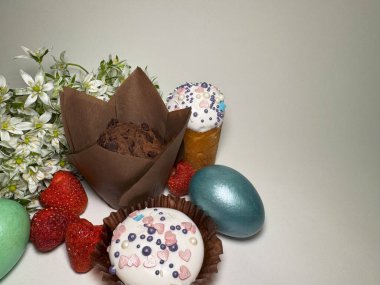 Süslü kapkekler, boyanmış yumurtalar, taze çilekler ve hafif arka planda bahar çiçekleri ile Paskalya kompozisyonu