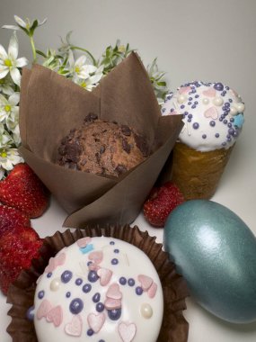 Kapkek, çikolatalı kek, renkli yumurta, çilek ve açık arkaplanda beyaz bahar çiçekleriyle bayramlık Paskalya kompozisyonu.