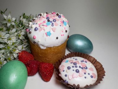 Paskalya pastası ve renkli süslemeli kurabiyeler, boyalı yumurtalar, taze çilekler ve temiz bir arka planda beyaz bahar çiçekleri.