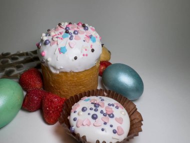 Traditional Easter cake with icing and colorful sprinkles, decorated cookies, dyed eggs, pussy willow branches, and fresh strawberries on a white background