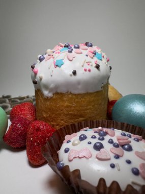 Easter cake with white icing and sprinkles, festive cookie, painted eggs, strawberries, and pussy willow branches on a white background