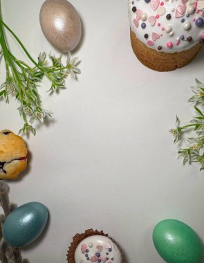 Paskalya bayramı çerçevesinin en üst görüntüsü pasta, kurabiye, yumurta ve bahar çiçekleriyle beyaz zemin üzerinde fotokopi alanı ile