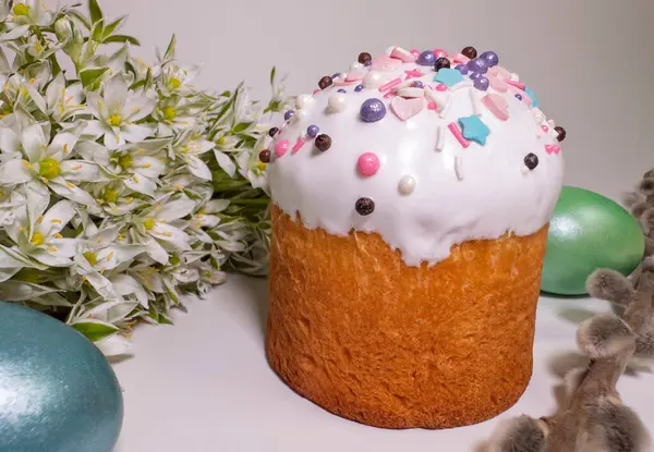 Traditional Easter cake with colorful sprinkles, painted eggs, white spring flowers, and pussy willow branches on a light background