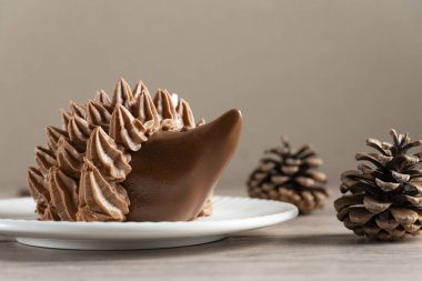 Çam kozalaklarıyla çevrili beyaz bir tabakta kirpi şeklinde çikolatalı bir tatlının yakın plan fotoğrafı.