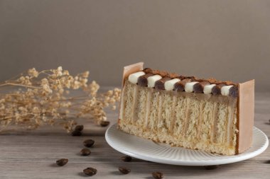 Çikolata kremalı, saçılmış kahve çekirdekleri ve ahşap bir yüzey üzerinde kurumuş çiçeklerle kaplı, kırsal tabakalı kahveli kekin yakın çekimi.