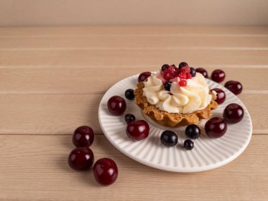 Çırpılmış krema ve taze böğürtlenlerle kaplı lezzetli bir kek, beyaz bir tabağa yerleştirilmiş, kirazlar ve kuşüzümü ile, ahşap bir arka planda. Gıda içeriği, menüler ve reklamlar için ideal