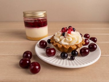 Kırsal ahşap arka planda çırpılmış krema ve taze böğürtlenli gevrek bir tartın yakın çekimi. Canlı ve iştah açıcı, mutfak, yaşam tarzı ve yemek fotoğrafçılığı temaları için ideal.