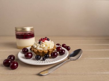 Kremalı turta ve kiraz, kaşık ve ahşap bir masada katmanlı tatlı kavanozu olan bir tabakta. Konforlu ve minimalist gıda seti