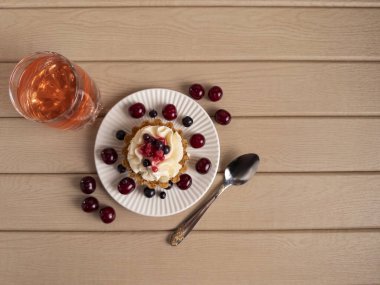 Krem şantili ve beyaz bir tabakta taze böğürtlenli, ahşap bir masada pembe bir içecek ve kaşıkla eşleştirilmiş bir tatlı manzarası.