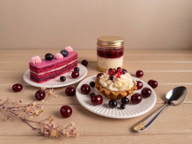 Beyaz tabakta taze böğürtlenlerle süslenmiş, bir kaşık ve kurumuş çiçeklerle süslenmiş, katmanlı pasta, tart ve bir kavanoz tatlının da dahil olduğu çok güzel bir tatlı çeşidi.